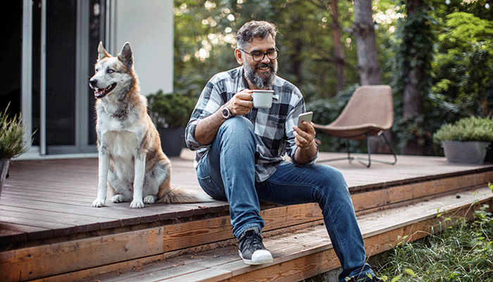 A man sits on a step of a back patio with a large dog next to him.