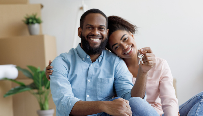 Glad cheerful young african american family show key and enjoy purchase of real estate in room with cardboard boxes.