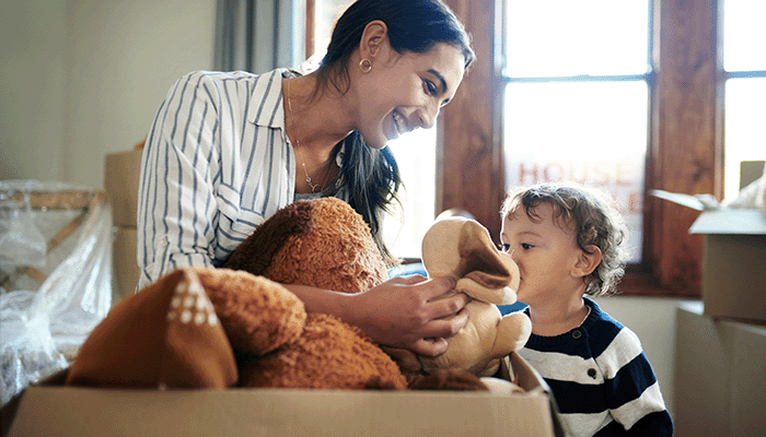 A mother and her young child unpacking a box of toys in a brightly lit room.