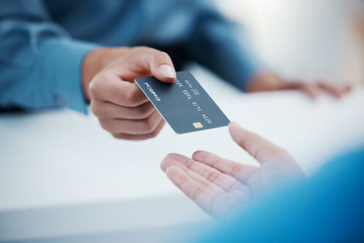 A close-up of a person's hands as they offer a credit card to someone else, symbolizing a payment or financial transaction.