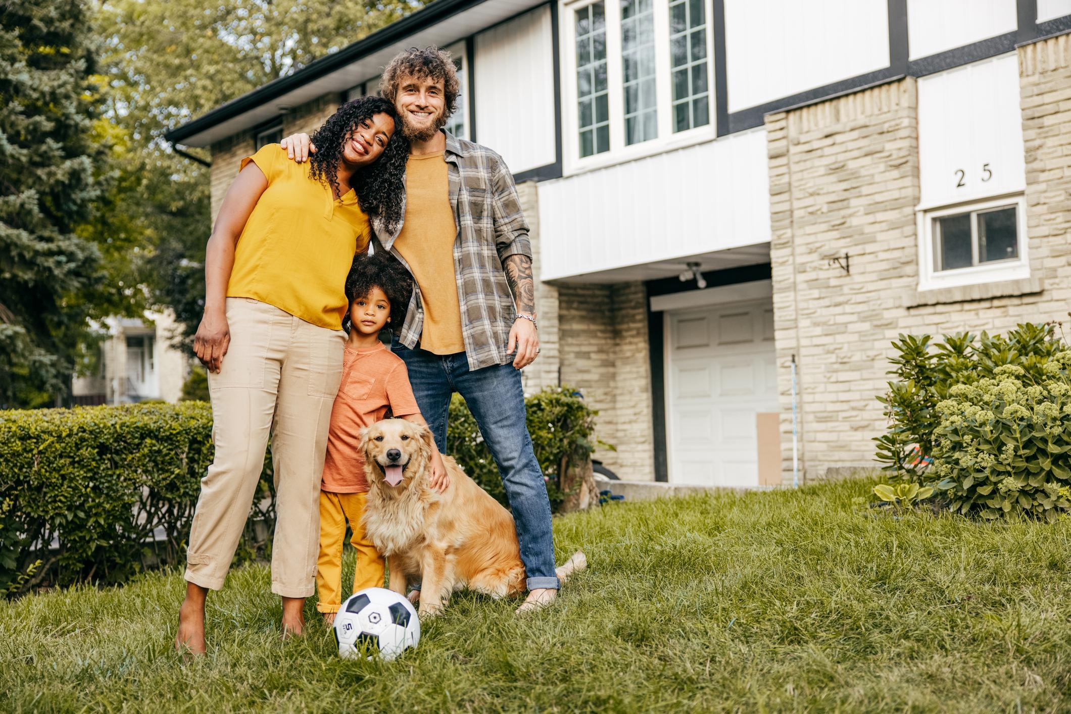 Multi-ethnical family and their dog in front of their house.
